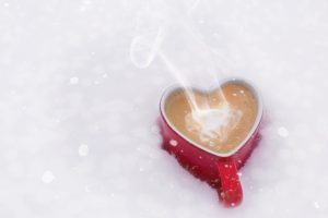 Tasse en forme de cœur remplie de café fumant, posée dans la neige